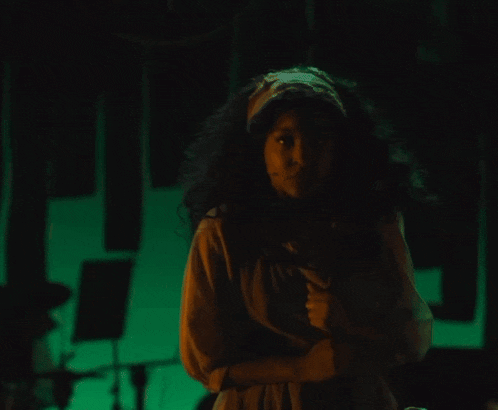 a woman stands in a dark room with a green light behind her