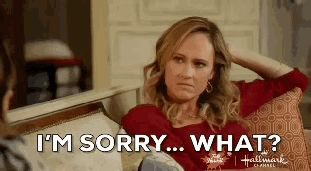 a woman is sitting on a couch with her hand on her head and saying `` i 'm sorry ... what ? ''