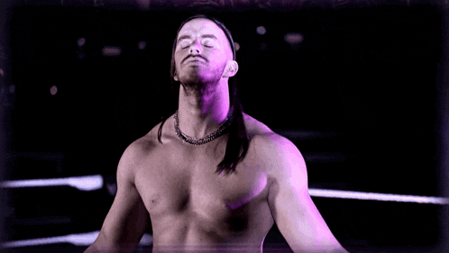 a man with a beard and long hair looks at the camera with purple lights behind him
