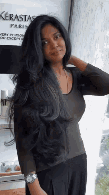 a woman with very long black hair is standing in front of a kerastase paris sign