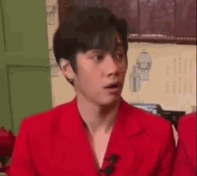 a man in a red jacket is making a funny face while sitting in a room .