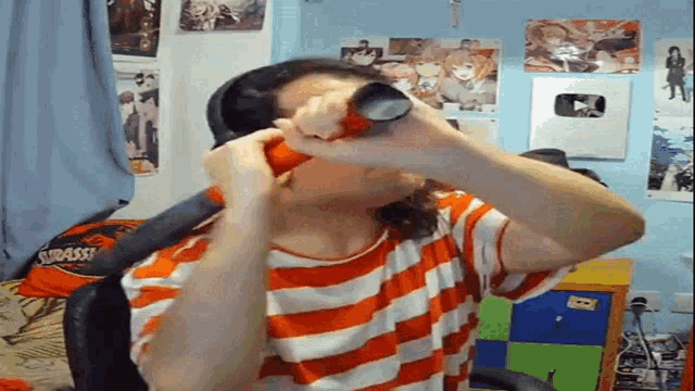 a person in an orange and white striped shirt is drinking from a can of soda .
