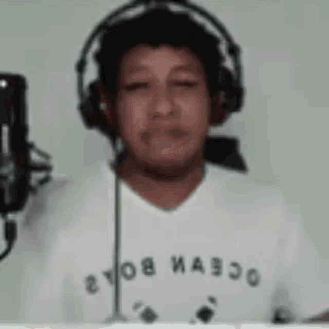 a man wearing headphones and a white shirt with the word ocean on it is singing into a microphone .