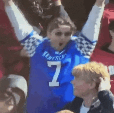 a man in a blue jersey with the number 7 on it is raising his arms in the air .