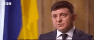 a man in a suit and tie is sitting in front of a flag .