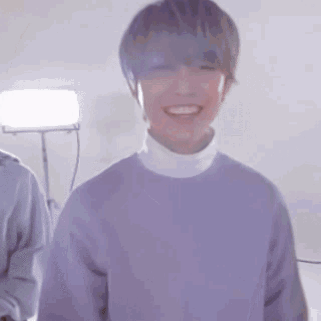 a man wearing a purple sweater and a white turtleneck smiles .