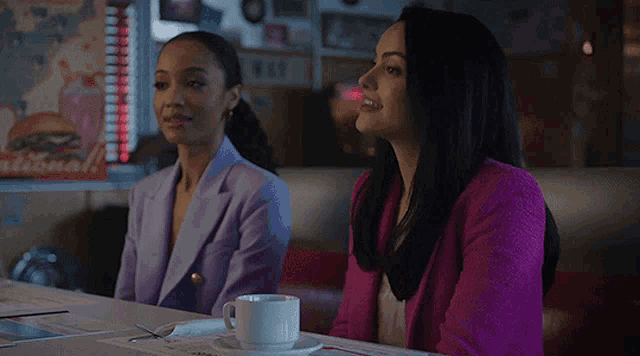 two women are sitting at a table with a cup of coffee and a menu .