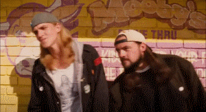 two men are standing in front of a brick wall with graffiti on it that says booby 's thru