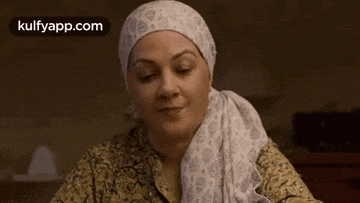 a woman wearing a turban and a scarf around her head is sitting at a table with her eyes closed .