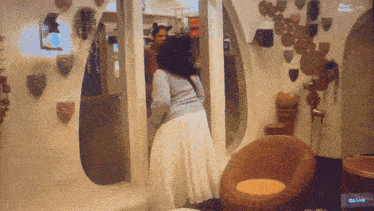 a woman in a white skirt stands in a room with a tv screen that says go live on it