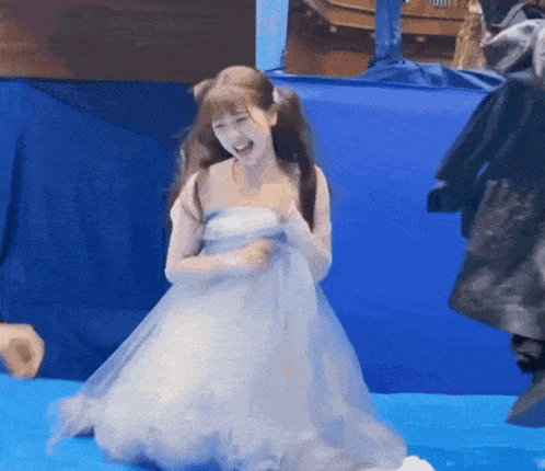 a woman in a white dress is laughing while kneeling on a blue mat
