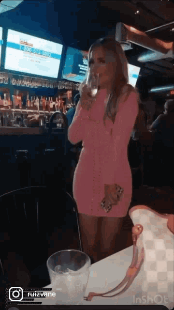 a woman in a pink dress drinking from a glass