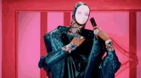 a woman in a blue dress and mask is holding a microphone in her hand .