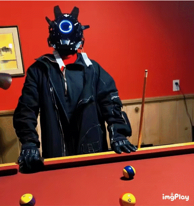 a man wearing a helmet stands on a pool table with pool balls