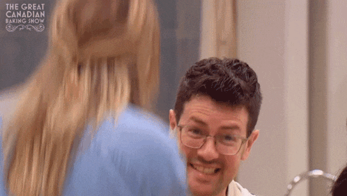 a man wearing glasses is smiling at a woman in a blue shirt in a kitchen .