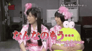 two girls are sitting next to each other and one has a stuffed frog on her lap
