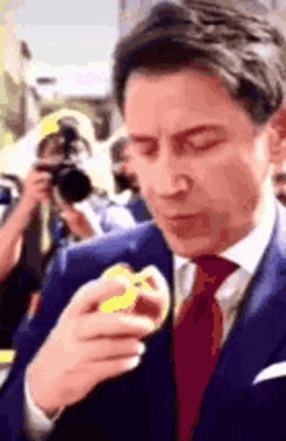 a man in a suit and tie is eating something while a cameraman takes a picture of him .