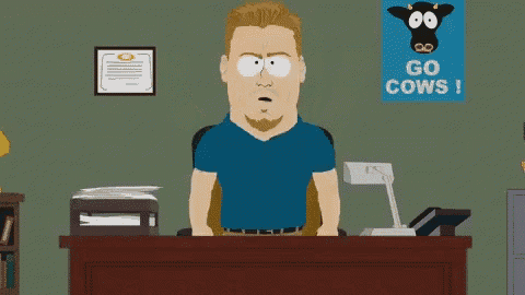 a man in a blue shirt is sitting at a desk in front of a sign that says go cows !