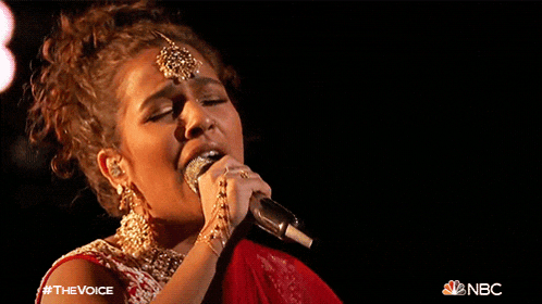 a woman singing into a microphone with a nbc logo in the corner