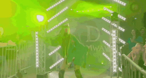 a woman in a green jacket is walking through a ring with the letter d on the wall