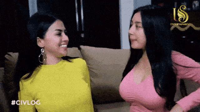 two women are sitting on a couch and one of them is wearing a yellow shirt