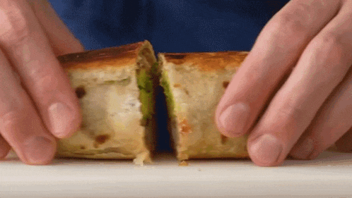 a person is cutting a sandwich in half on a white cutting board