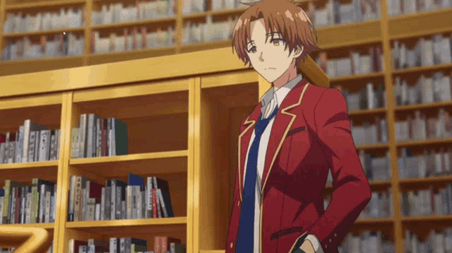a man in a red suit and tie stands in front of a bookshelf