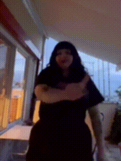 a woman with long black hair is standing with her arms crossed in a room .