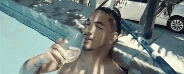 a shirtless man is laying in a swimming pool holding a glass of wine .