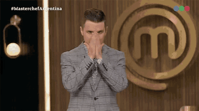 a man in a suit covering his face in front of a masterchef logo