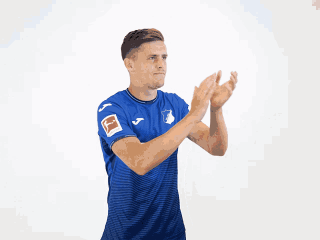 a man wearing a blue shirt with the word tsg on it applauds