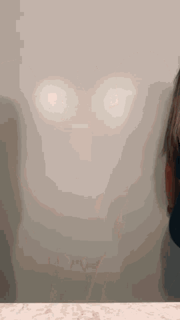 a woman standing in front of a wall with a shadow of a face on it