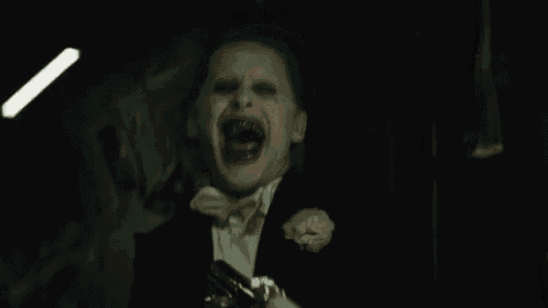the joker is wearing a tuxedo and a bow tie and is screaming in the dark .