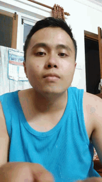a man in a blue tank top looks at the camera with a calendar behind him