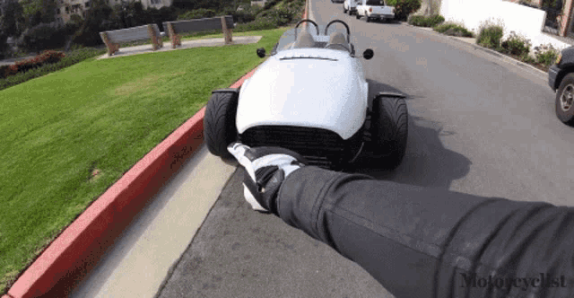 a white sports car is parked on the side of the road next to a grassy hill