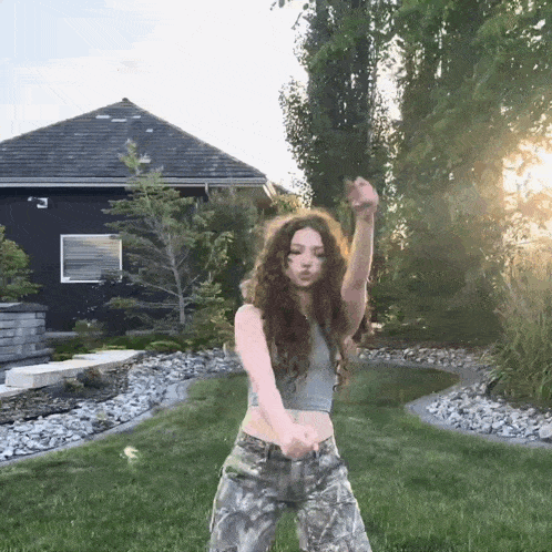 a girl in a crop top and camo pants is dancing in a yard