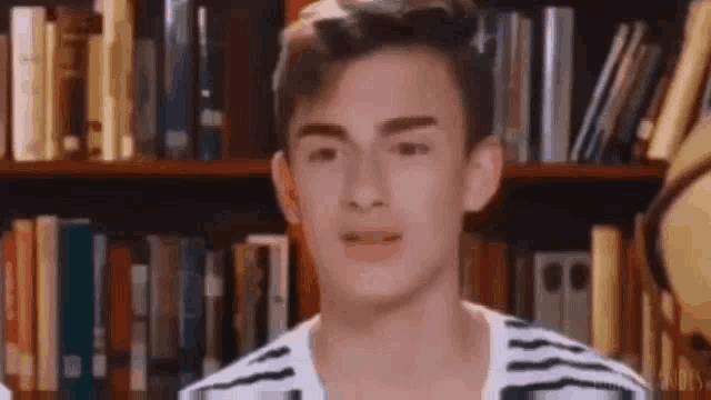 a young man is standing in front of a bookshelf with books on it .