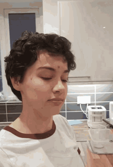 a woman with short curly hair is standing in a kitchen