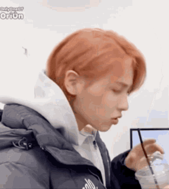 a person with red hair is holding a cup of coffee and a straw .