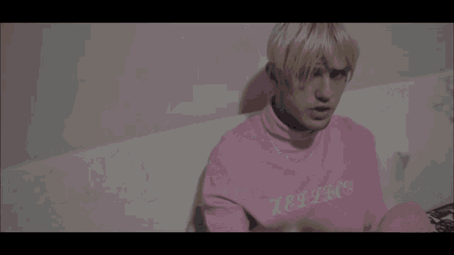 a man wearing a pink sweatshirt is making a heart with his hands
