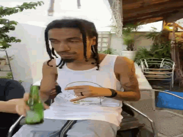a man with dreadlocks and a ring on his finger holds a green bottle