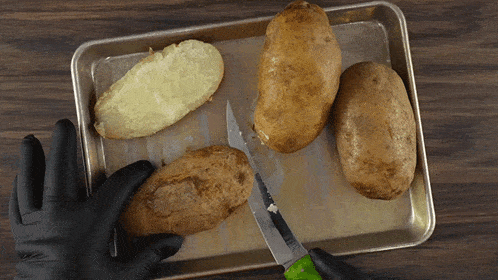 a person wearing black gloves is cutting a potato on a pan