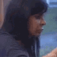 a woman with long black hair is sitting at a table looking at her phone .