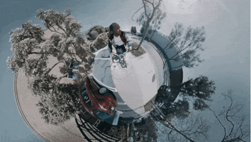 a person riding a bike in a circle with trees and a car that has the letter t on it