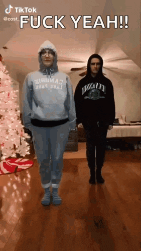 two people are standing next to each other in front of a christmas tree and a sign that says fuck yeah !