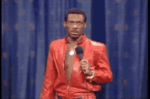 a man in a red suit stands in front of a microphone with the word that above him