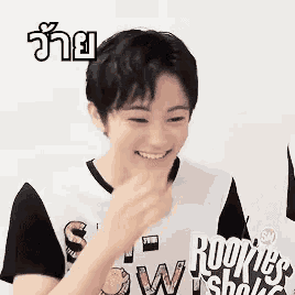 a young man wearing a rookie 's world shirt is smiling and eating something .