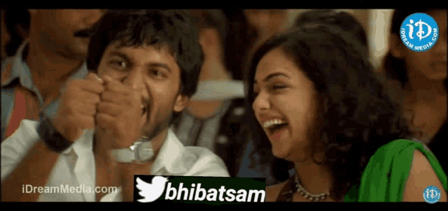 a man and a woman are laughing in a crowd with a twitter logo behind them