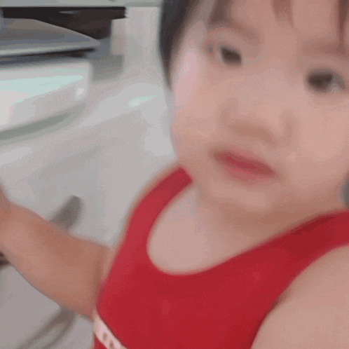 a little girl in a red tank top is looking at the camera