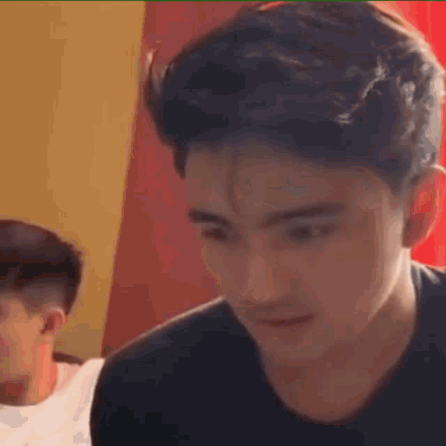a young man in a black shirt is making a funny face while sitting at a table .